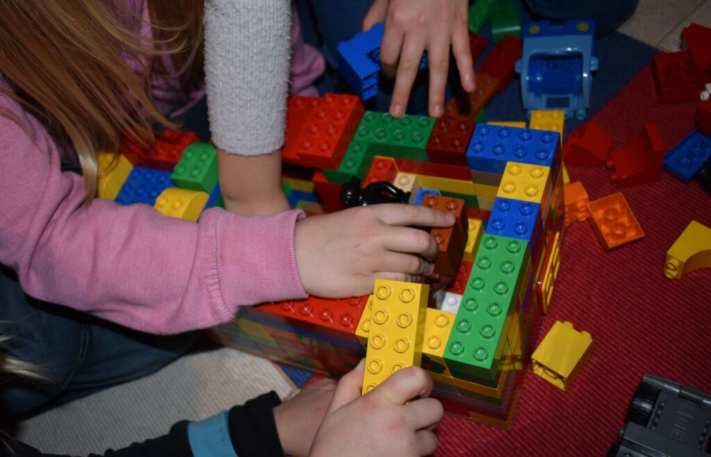 Mehrere Kinderhände spielen an einem Bauwerk aus Plastik-Klemmbausteinen