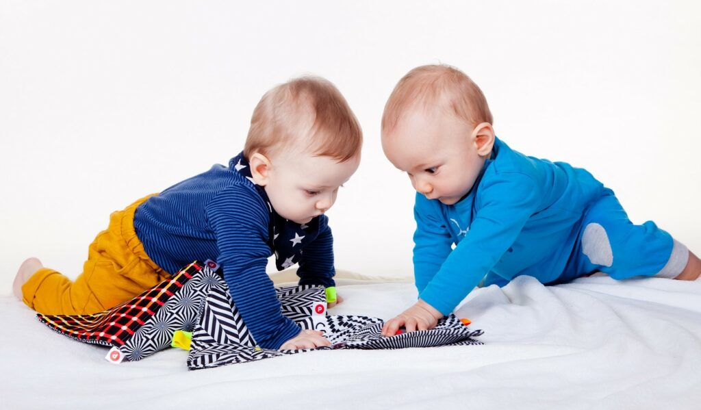 Zwei Babys spielen auf einer Decke mit verschiedenen Textilien