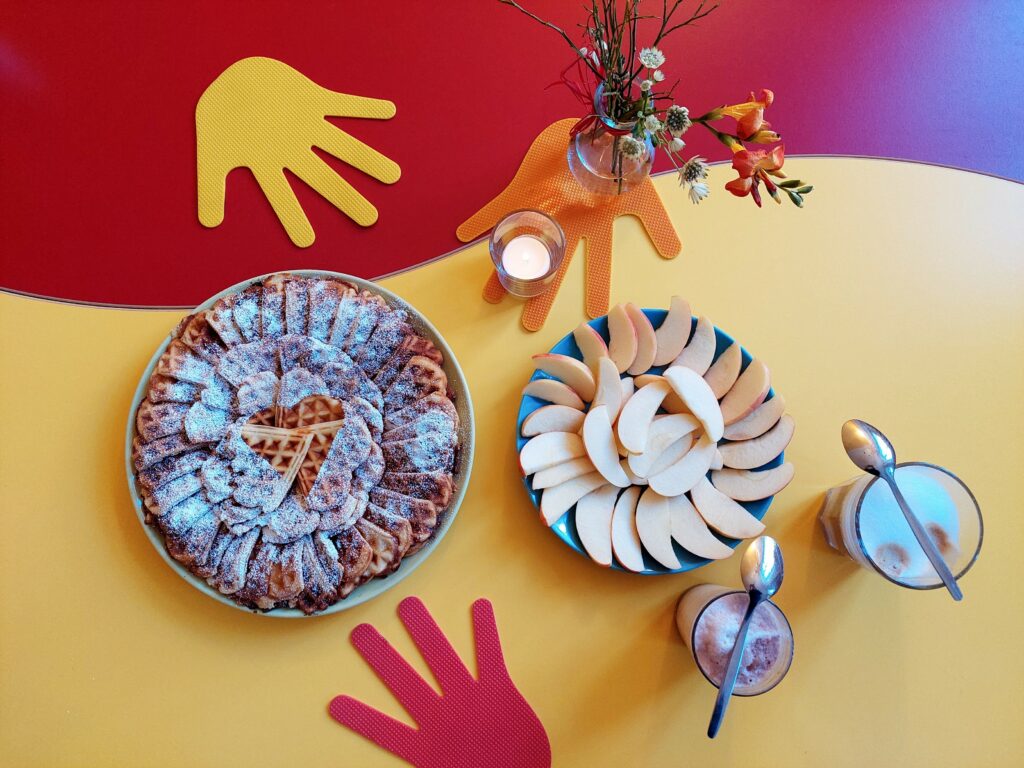 Ein Teller mit Apfelspalten, ein weiterer Teller mit Waffelstücken sowie zwei Getränke stehen auf einem dekorierten Tisch